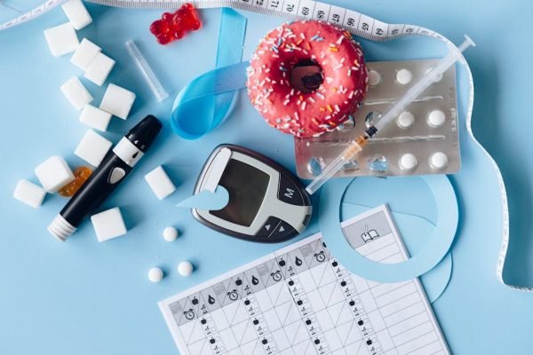 pexels-photo-6942015-6942015 Still life image of diabetes management equipment, sweets, and medication arranged artfully on a blue background.