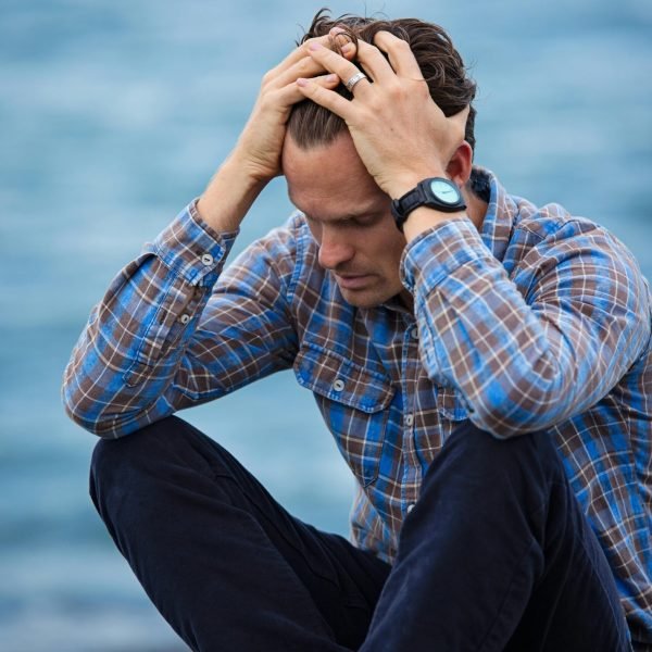 pexels-photo-897817-897817 A man in a plaid shirt sits by the water looking distressed, symbolizing stress.